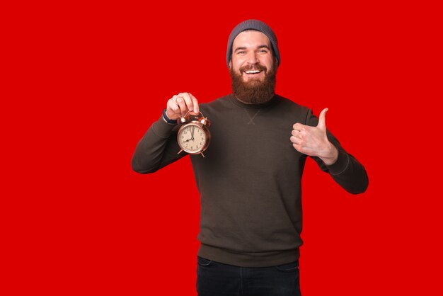 Photo d'un homme à la barbe tenant un réveil et montrant le pouce vers le haut