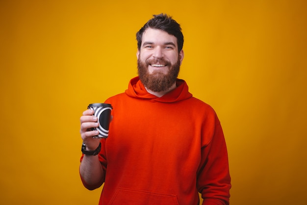 Photo d'un homme barbu sur l'espace jaune tient un papier café noir et blanc pour aller tasse.