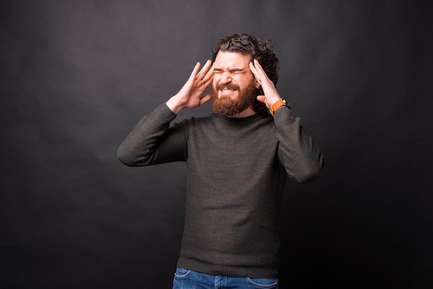 Photo d'un homme barbu frustré tenant sa tête sur fond noir