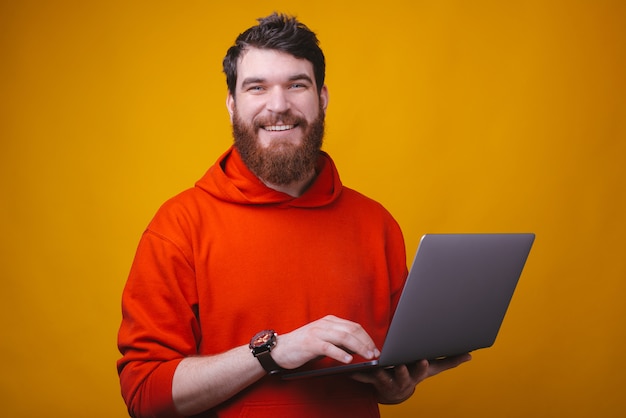 Photo d'un homme barbu gai tenant un ordinateur portable, commandant ou travaillant en ligne ou surfant sur Internet.