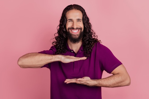 Photo d'un homme brun agréable tenir un espace vide mesurer une petite taille porter un t-shirt violet isolé sur fond de couleur rose