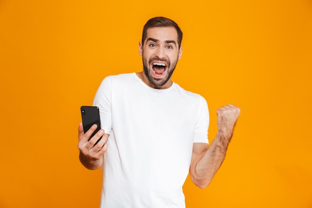 Photo d'un homme brune de 30 ans en tenue décontractée criant et tenant un smartphone, isolé