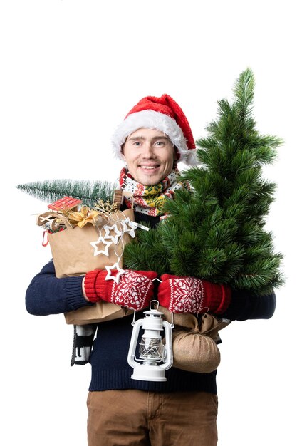 Photo d'un homme en casquette de père Noël avec des boîtes d'arbres de Noël avec des cadeaux en papier d'emballage dans les mains