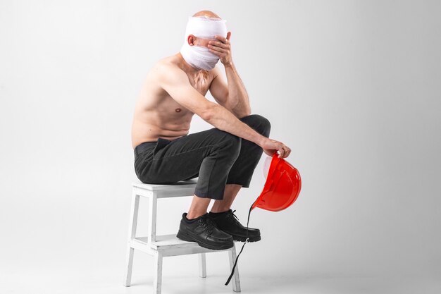 Photo d'un homme désespéré avec une tête bandée est assis sur une chaise avec un casque de protection