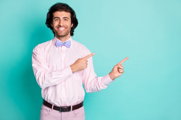 Photo d'un homme doux rayonnant à pleines dents porter une tenue rose pointant deux doigts sur un espace vide isolé sur fond de couleur turquoise