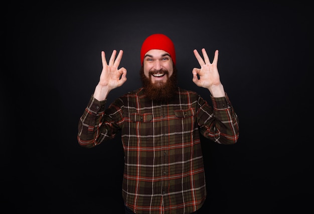 Photo d'un homme gai avec barbe et chapeau rouge faisant signe ok sur un mur sombre isolé