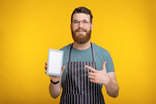 Photo d'un homme gai chef debout sur jaune et pointant sur tablette écran