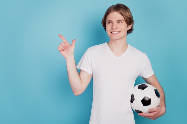 Photo d'un homme gai pointer du doigt l'espace vide tenant un ballon de football fond bleu isolé