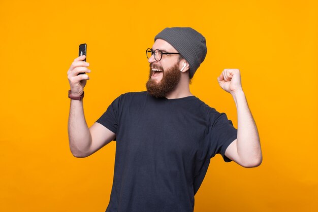 Photo d'un homme hipster barbu étonné regardant smartphone et célébrant