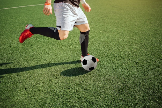 Photo d'un homme jouant au football. Il va botter le ballon. Guy joue seul sur le terrain. Le soleil brille dehors. Vue en coupe.