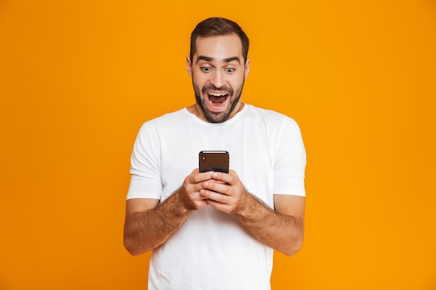 Photo d'un homme joyeux de 30 ans en tenue décontractée souriant et tenant un smartphone, isolé