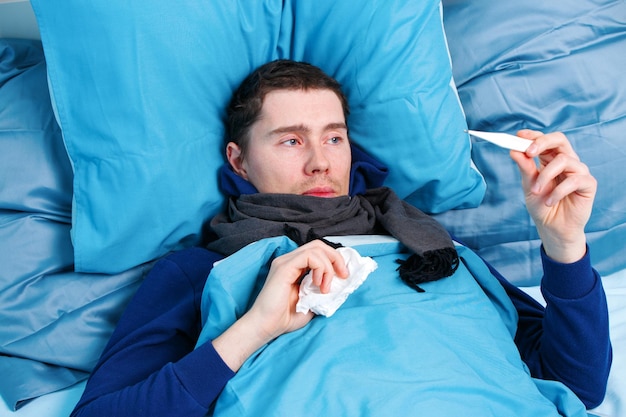 Photo d'un homme malade en écharpe avec thermomètre à la main couché dans son lit