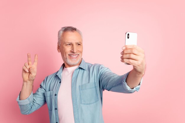 Photo d'un homme mûr shoot selfie cellphone show doigts paix cool v-symbol isolé sur fond de couleur rose.