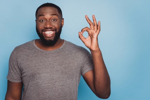 Photo d'un homme noir souriant donnant signe ok fond bleu isolé