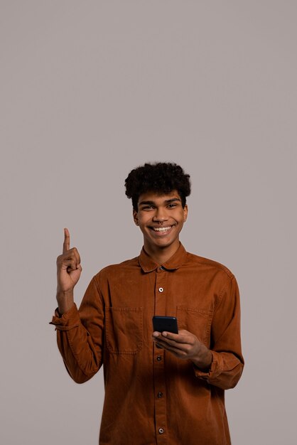 La photo d'un homme noir tient les smartphones et pointe vers le haut, a l'air bien. Homme porte chemise, fond de couleur grise isolé.