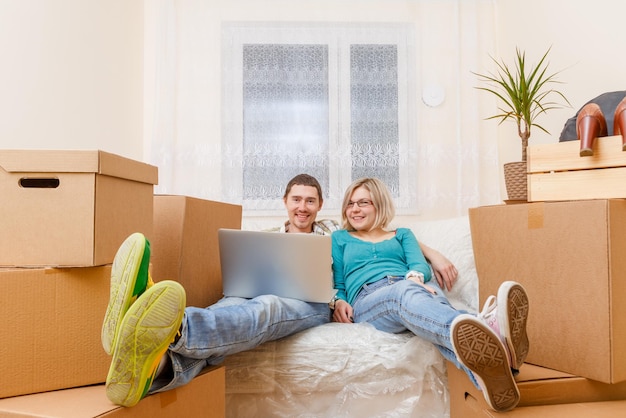 Photo d'un homme avec un ordinateur portable et une femme assise sur un canapé parmi des boîtes en carton