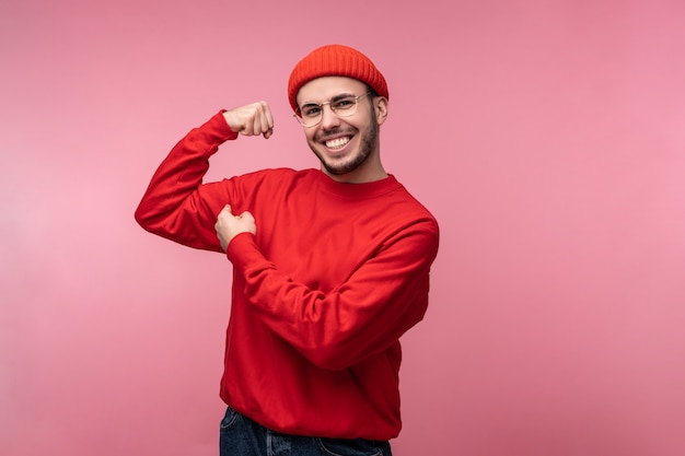 Photo d'un homme séduisant avec barbe à lunettes et vêtements rouges. Les hommes montrent des muscles forts et, isolés sur fond rose.