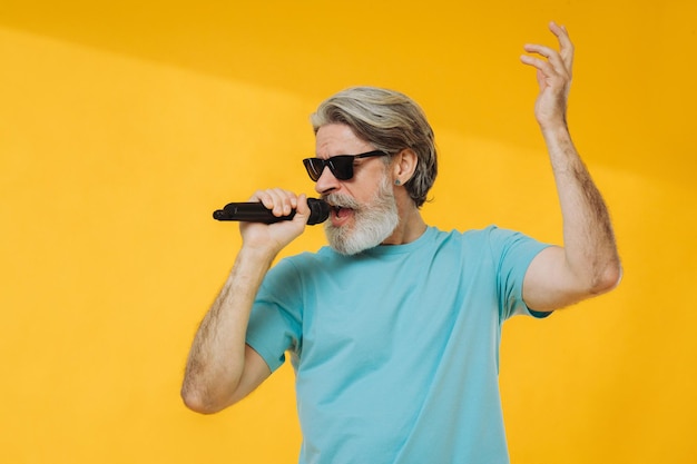 Photo d'un homme senior aux cheveux gris chantant portant des lunettes t-shirt bleu isolé sur fond jaune