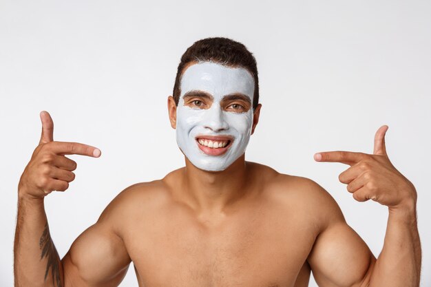 Photo d'un homme torse nu souriant et appliquant une crème pour le visage isolé sur blanc