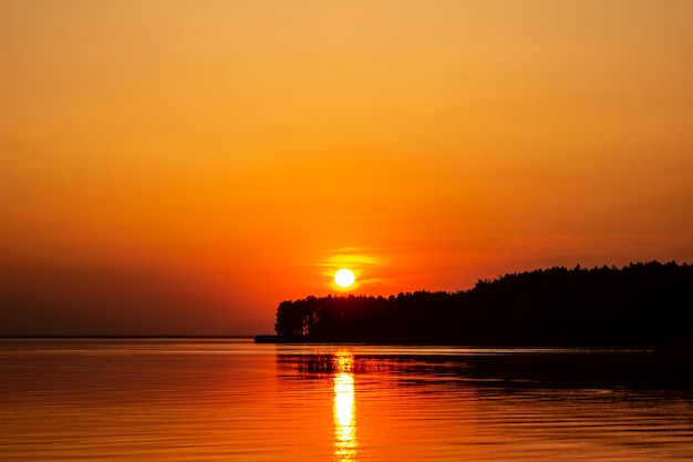 Photo la photo horizontale du coucher de soleil doré au-dessus de la rivière ou de la mer. reflet dans l'eau comme le feu. littoral.