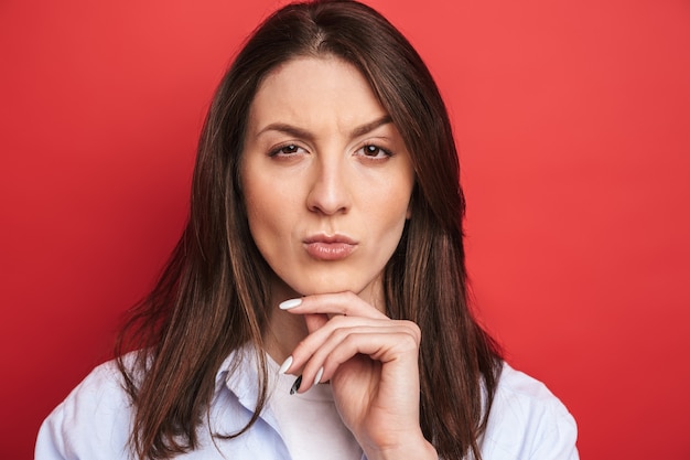 Photo d'une incroyable belle jeune femme sérieuse posant isolée sur un mur rouge.