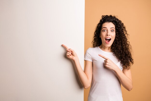 Photo de l'incroyable dame excitée indiquant le doigt sur la bannière de remise vide grande pancarte blanche porter des vêtements décontractés blancs fond de couleur pastel beige isolé