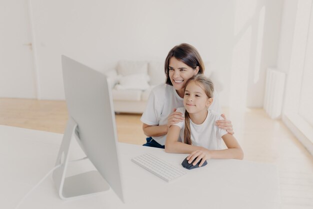 Photo à l'intérieur d'une mère et d'une fille heureuses et charmantes qui regardent un dessin animé drôle sur ordinateur ont des sourires agréables profitent de la convivialité passent du temps libre ou un week-end à la maison spacieux salon vide et lumineux