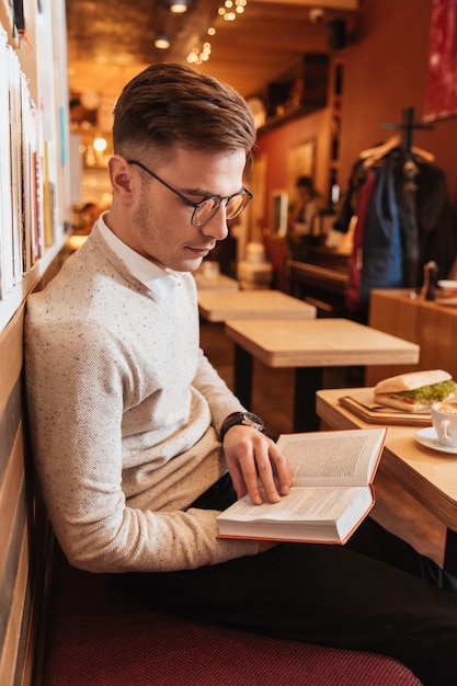 Photo de jeune bel homme assis dans un café en lisant un livre.