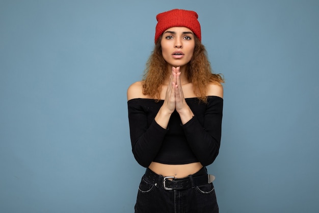 Photo de jeune belle femme brune bouclée avec des émotions sincères portant un crop top noir et rouge