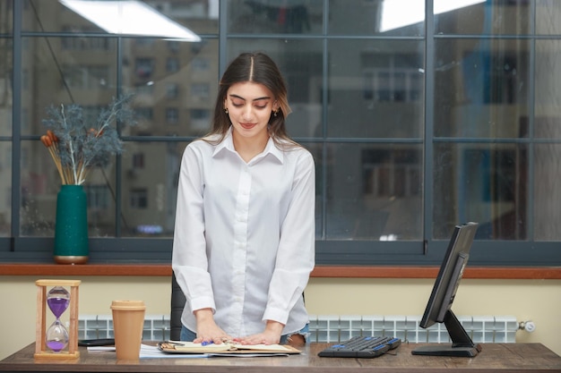 Photo de jeune belle fille debout au bureau et regardant son cahier