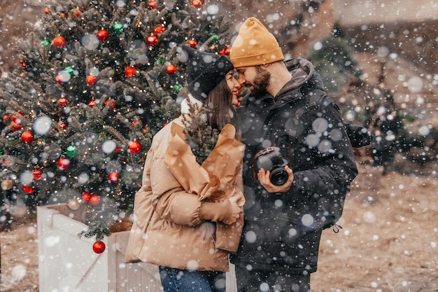 Photo d'un jeune couple amoureux élégant posant pour une photo lors d'une légère chute de neige à la foire de rue de Noël