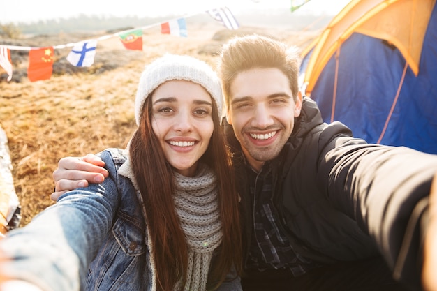 Photo d'un jeune couple d'amoureux heureux à l'extérieur dans des vacances alternatives gratuites en camping sur les montagnes, prendre un selfie par caméra