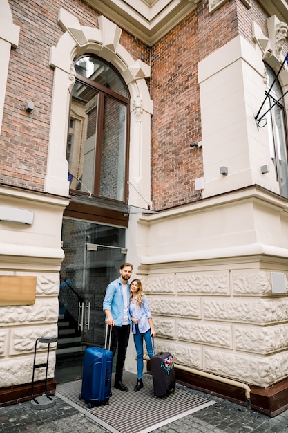 Photo d'un jeune couple entrant dans l'hôtel. Jeune, femme, debout, vieux, bâtiment, ville, hôtel, Dehors, tenue, valises