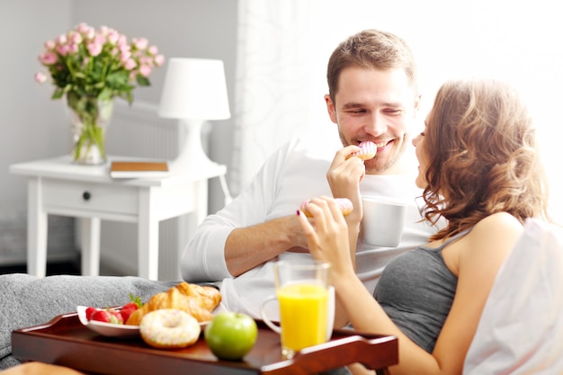 Photo de jeune couple mangeant le petit déjeuner au lit