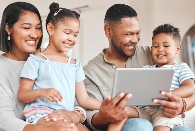 Photo d'une jeune famille se liant joyeusement tout en utilisant une tablette numérique ensemble sur le canapé à la maison