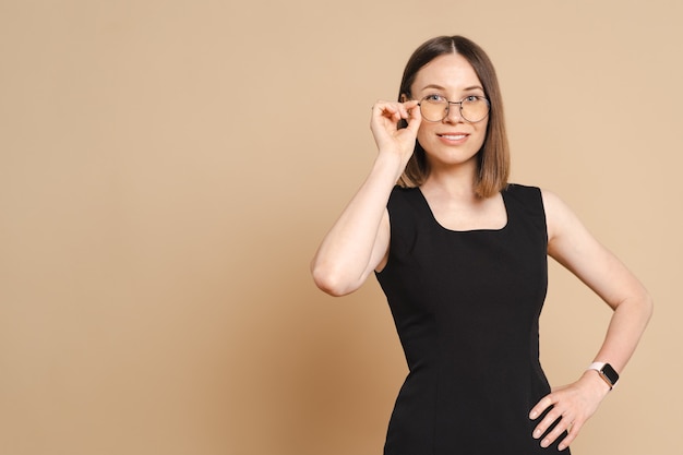 Photo d'une jeune femme d'affaires caucasienne heureuse portant des lunettes debout sur un mur beige