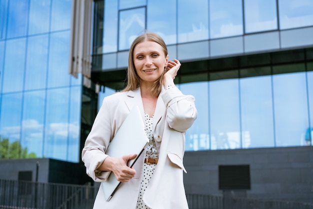 Photo de jeune femme d'affaires gaie caucasienne debout sur fond d'un immeuble de bureaux i...
