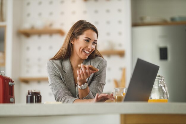 Photo d'une jeune femme d'affaires multitâche surfant sur les réseaux sociaux et prenant un petit-déjeuner à la maison tout en se préparant à aller travailler.