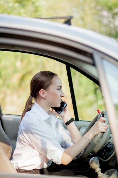 Photo de jeune femme d'affaires parle par téléphone et se maquille en conduisant une voiture dans les embouteillages