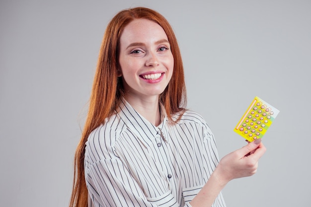 Photo de jeune femme d'affaires rousse en chemise rayée avec un paquet de pilules studio fond blanc