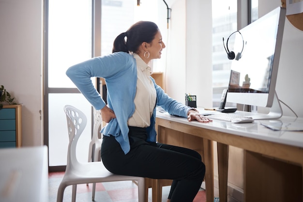 Photo d'une jeune femme d'affaires souffrant de maux de dos alors qu'elle travaillait à son bureau dans un bureau moderne