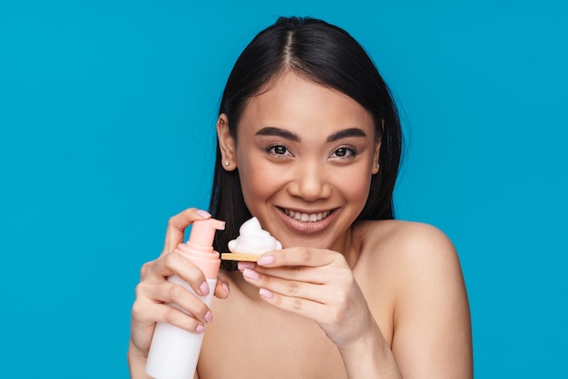 Photo d'une jeune femme asiatique optimiste et joyeuse posant isolée sur un mur bleu tenant une mousse nettoyante en mousse.