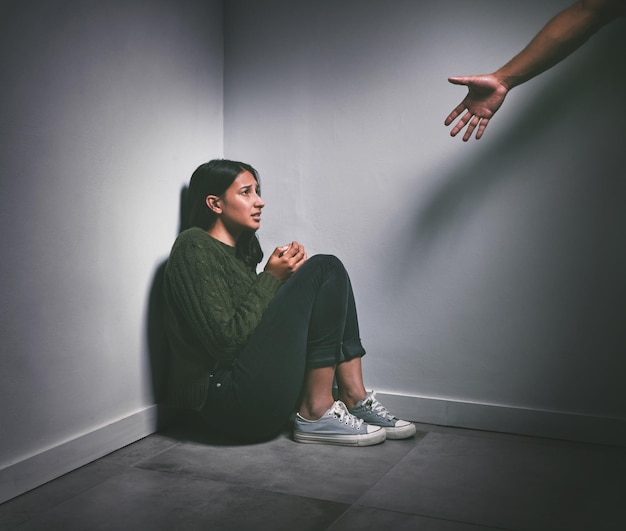 Photo d'une jeune femme assise dans le coin d'une pièce sombre avec une main tendue pour l'aider