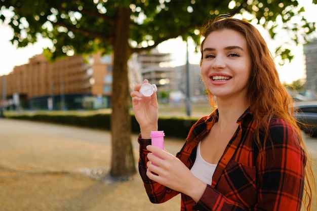 Photo d'une jeune femme aux cheveux roux heureux souriante portant une chemise ordinaire soufflant des bulles d'air debout dans le