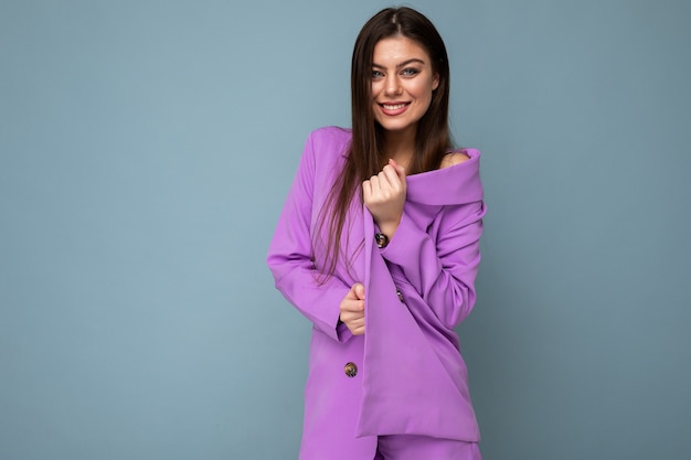 Photo d'une jeune femme brune aux cheveux longs positive portant un costume violet isolé sur fond bleu. Espace de copie