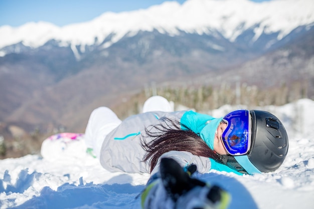 Photo de jeune femme en casque et avec snowboard allongé sur la pente de la montagne