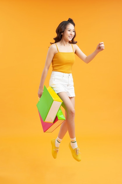 Photo de jeune femme émotive marchant isolée sur fond de mur jaune tenant des sacs à provisions.