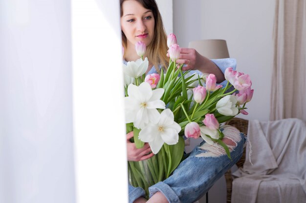 Photo de jeune femme est assise sur une fenêtre avec un bouquet de fleurs