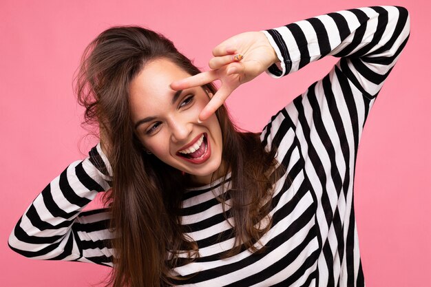 Photo d'une jeune femme européenne souriante positive et séduisante, heureuse et charmante, avec des émotions sincères, portant un pull rayé décontracté isolé sur fond rose avec espace de copie.