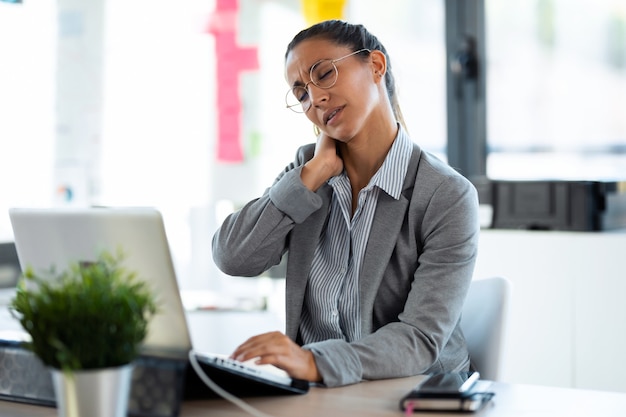 Photo d'une jeune femme fatiguée souffrant de douleurs au cou travaillant avec son ordinateur au bureau